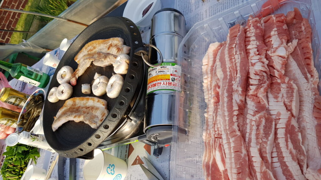 A mouth-watering close-up of thick slices of Korean pork belly (Samgyeopsal) grilling and sizzling to a perfect golden brown on a hot plate 07