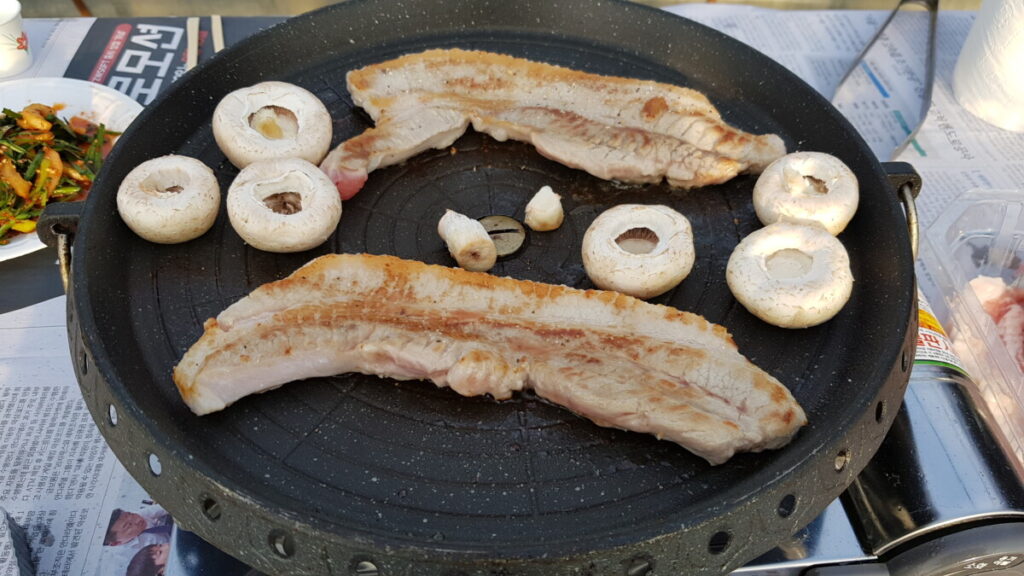 A mouth-watering close-up of thick slices of Korean pork belly (Samgyeopsal) grilling and sizzling to a perfect golden brown on a hot plate 05