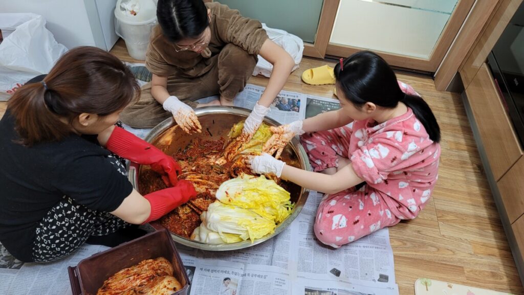 A family gathering in a cozy indoor kitchen to make traditional Korean kimchi together.