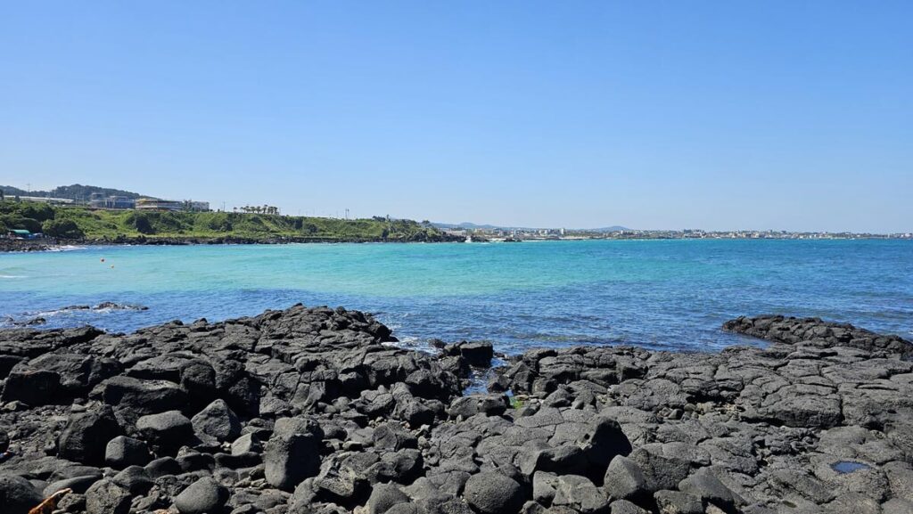 A beautiful panoramic view of the emerald blue ocean waves hitting the coastline of Jeju Island under a clear sky.