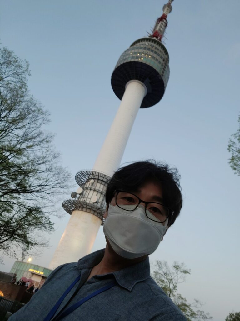 K-papa posing happily with the iconic Namsan Seoul Tower standing tall in the background.