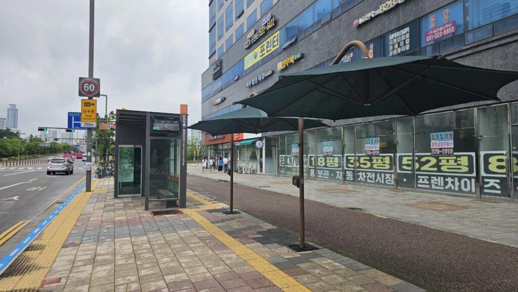 A giant smart cooling sunshade umbrella installed near a Korean bus stop to protect pedestrians from the hot summer heat.