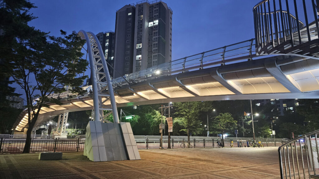 A warm and cozy neighborhood pedestrian bridge at night illuminated by streetlights and built-in landscape lighting.