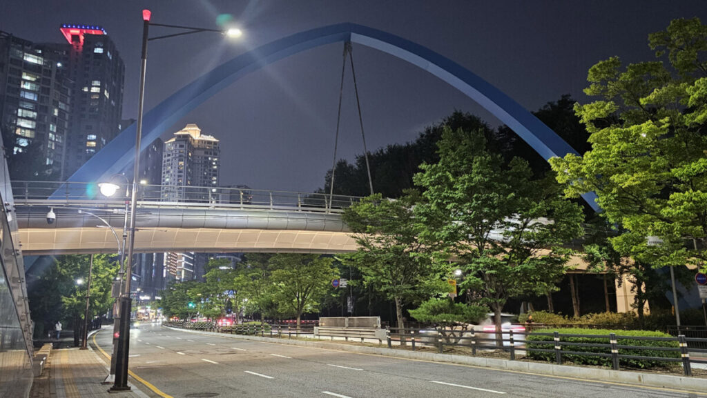 A quiet pedestrian walkway on top of a modern overpass bridge glowing under subtle evening lights.