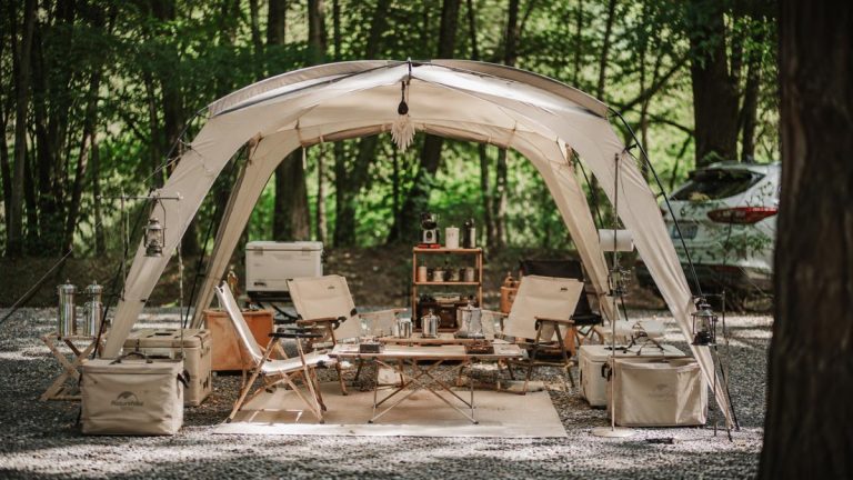 Floorless shelter used as an outdoor living space at a Korean-style campsite with tables, chairs, and camping equipment