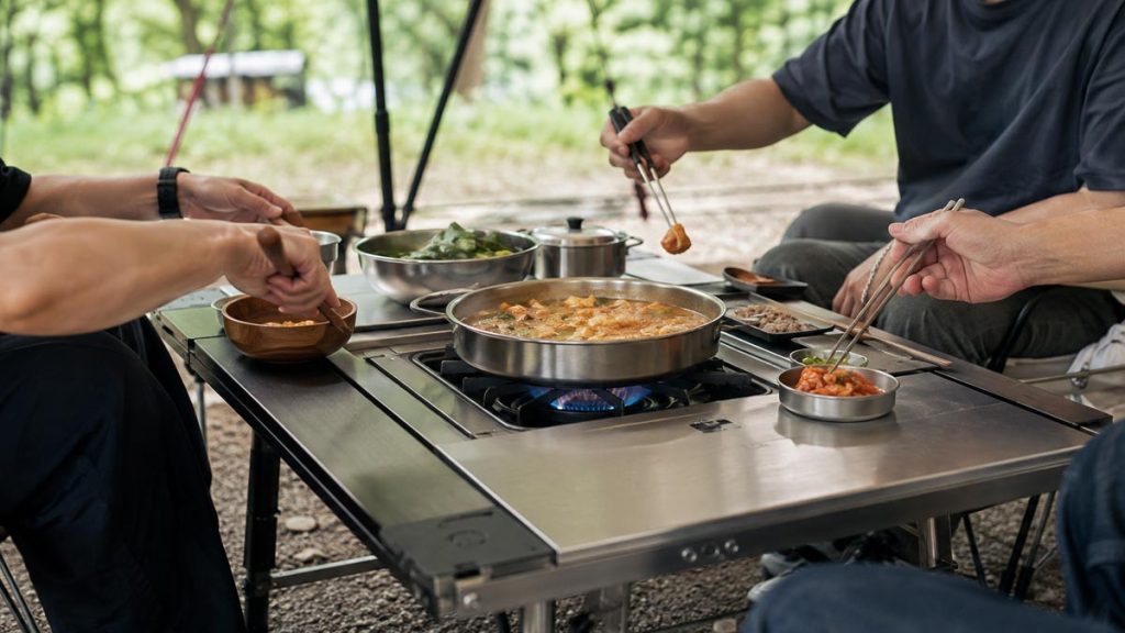 Campers sharing Korean food cooked on a burner integrated into an IGT table
