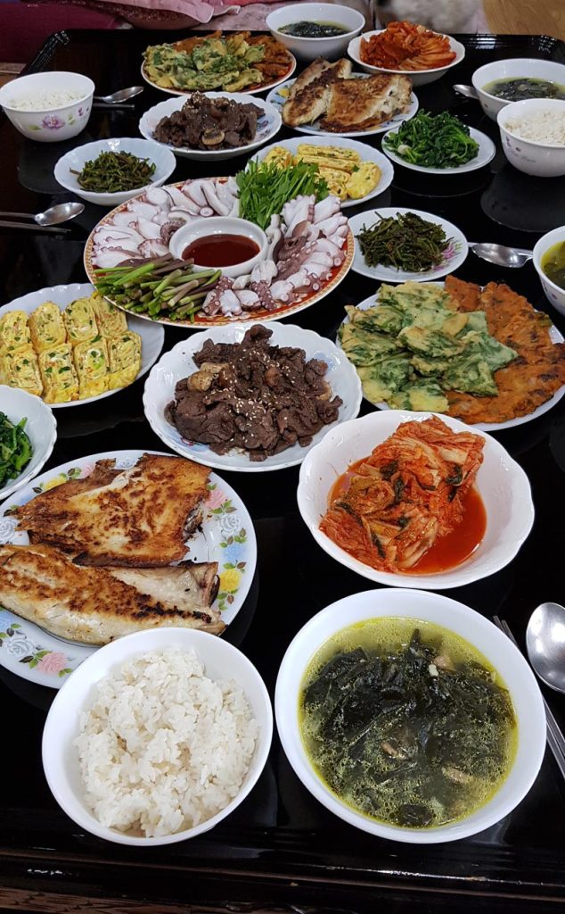 Home-cooked Korean meal with banchan, grilled fish, bulgogi, octopus, kimchi, egg rolls, and seaweed soup