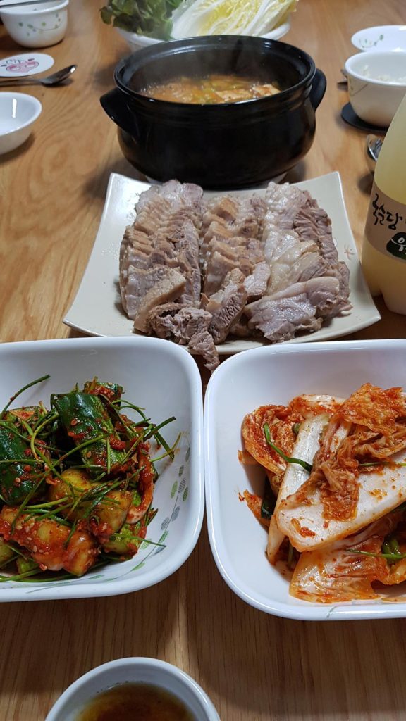 Korean boiled pork suyuk served with kimchi and doenjang jjigae in a black earthenware pot