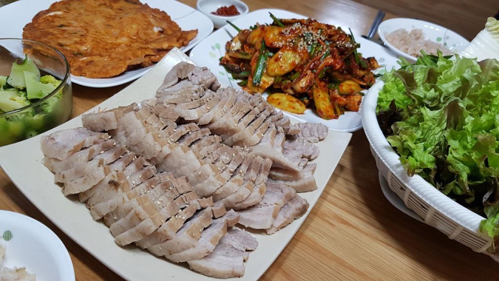 Korean boiled pork suyuk served with lettuce, seasoned vegetables, broccoli, and homemade side dishes on a family table