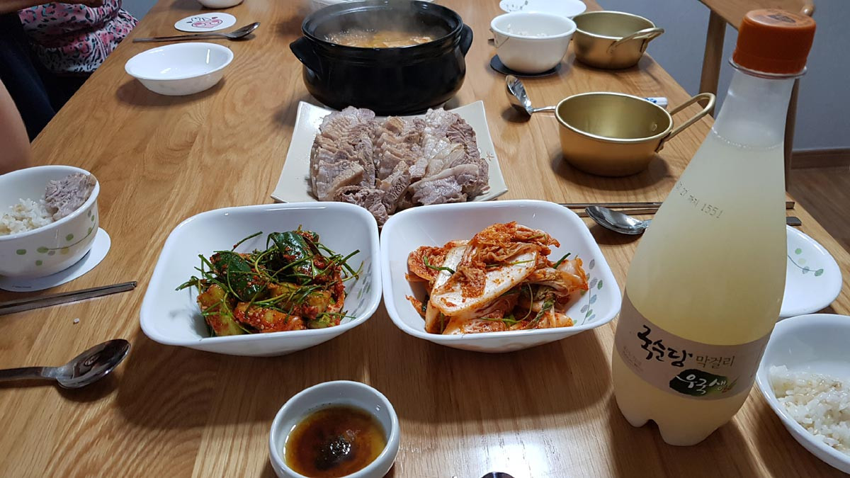 Homemade Korean boiled pork suyuk served with geotjeori, doenjang jjigae, rice, and makgeolli at a Korean family table