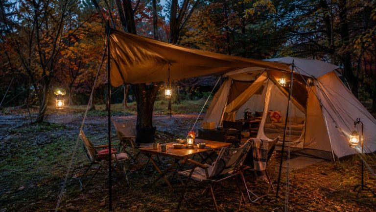 Korean campers' outdoor living room with warm lanterns, wooden table, chairs, and a tent in an autumn forest campsite