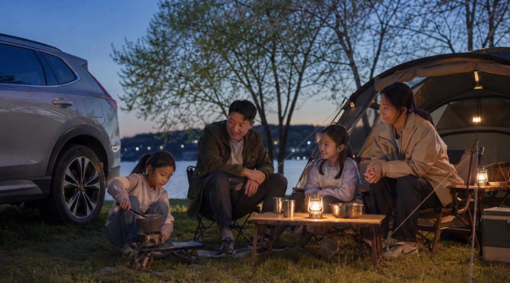 Korean family car camping beside a peaceful lake as parents and children relax together at dusk