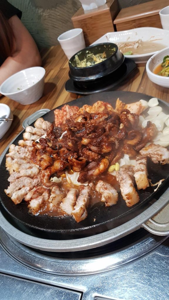 Grilled Korean pork belly and spicy octopus cooking together with kimchi, onions, and garlic