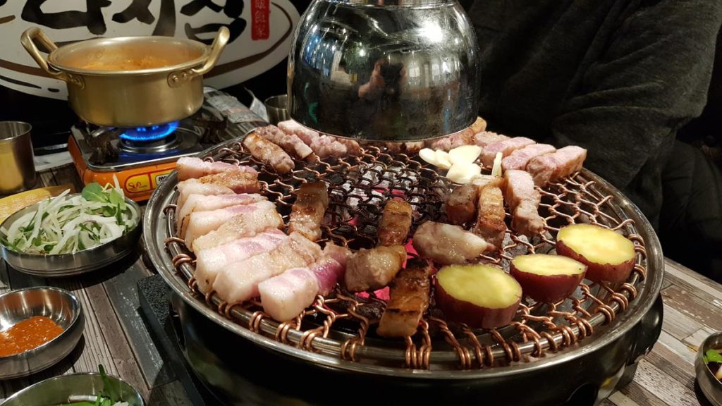 Korean samgyeopsal grilling over charcoal with garlic and sweet potatoes at a Korean BBQ restaurant