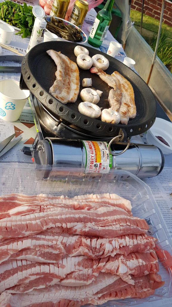 Thick slices of Korean samgyeopsal grilling with mushrooms during an outdoor Korean BBQ meal