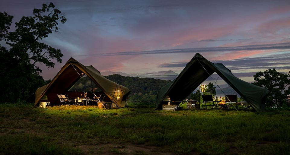 Minimal Works Superposition shelters in two colors set up at a campsite during sunset