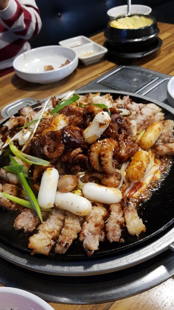 Samgyeopsal served with spicy grilled octopus, rice cakes, green onions, and garlic on a Korean BBQ grill