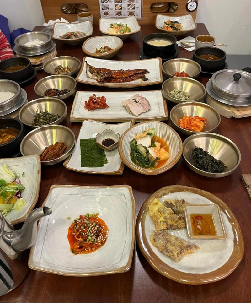 Traditional Korean restaurant table filled with banchan, grilled fish, kimchi, vegetables, rice, and soup