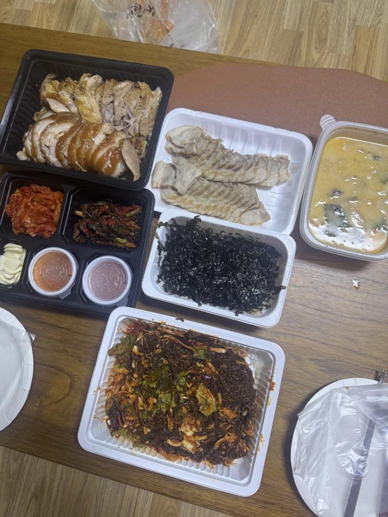 Korean delivery meal with sliced jokbal, bossam pork, spicy makguksu, seaweed, kimchi, and soup
