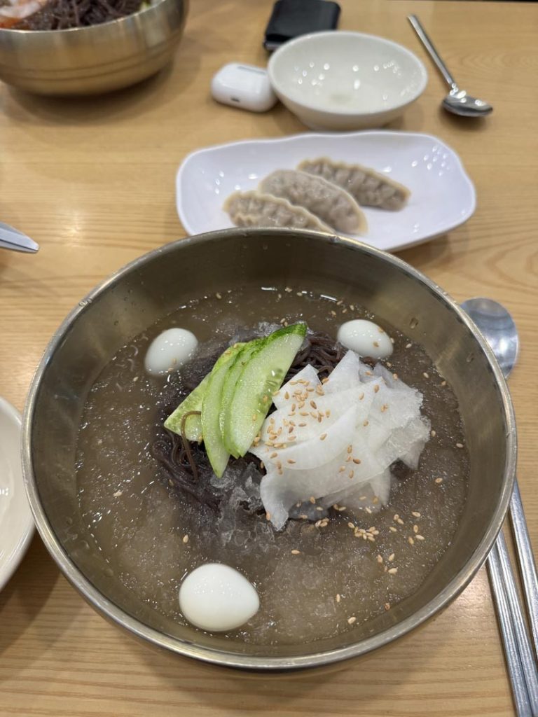 Korean mul naengmyeon in cold broth topped with cucumber, sliced radish, sesame seeds, and quail eggs.