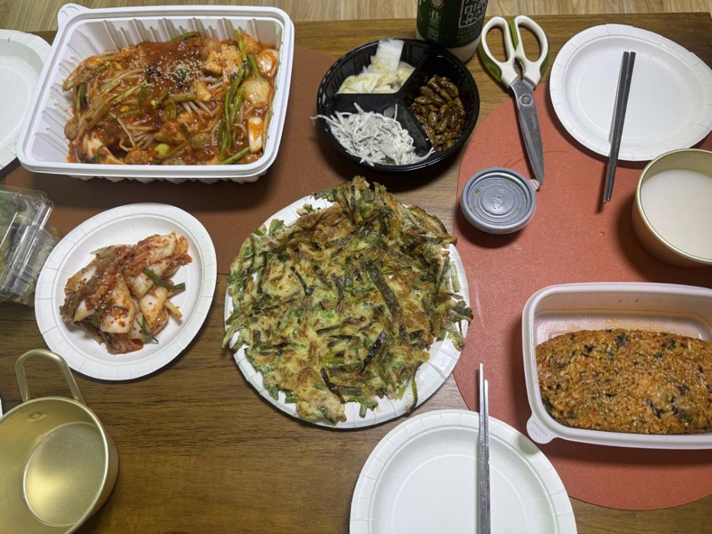 Korean delivery meal with spicy braised seafood, haemul pajeon, fried rice, kimchi, and side dishes on a dining table