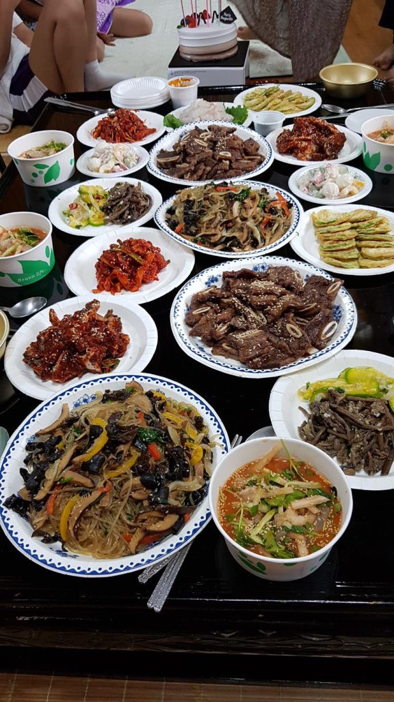 A large Korean home-cooked birthday meal with galbi, japchae, jeon, salads, and other shared dishes.