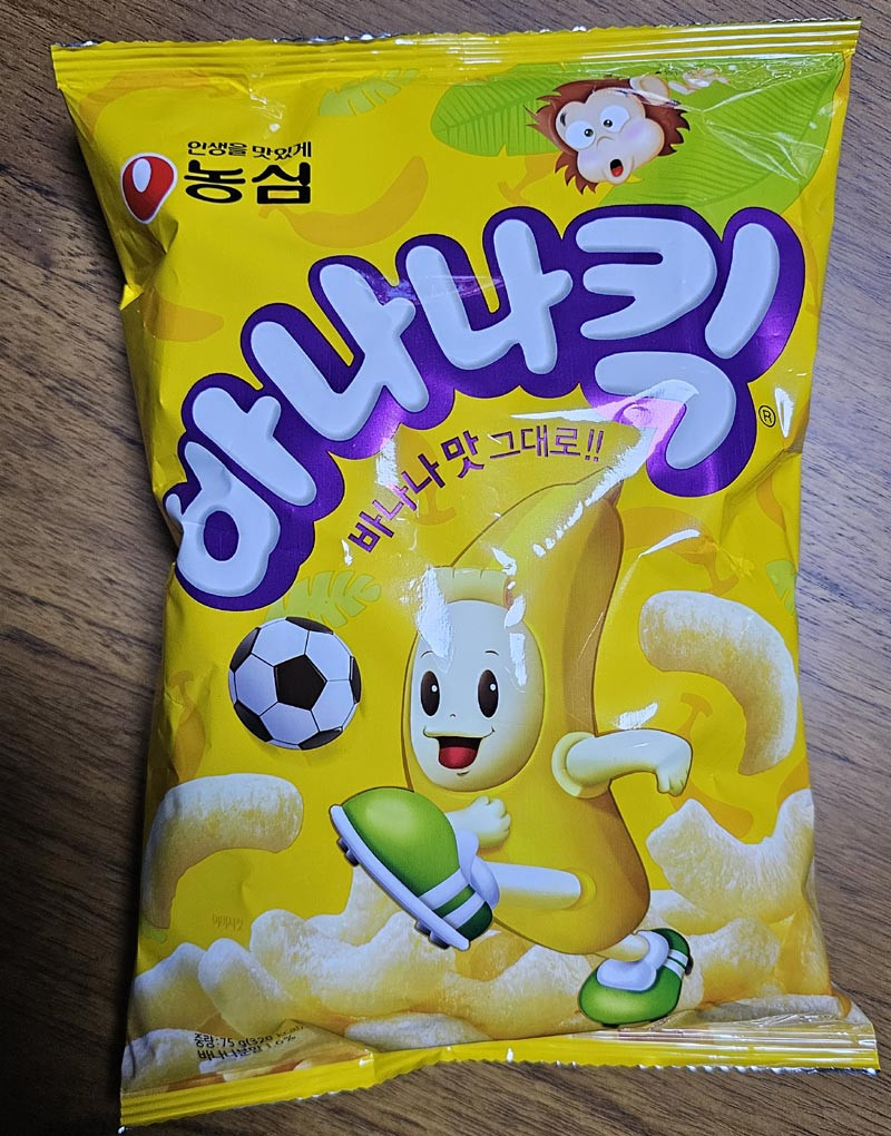 Front of a yellow Nongshim Banana Kick snack bag with its banana character and corn puffs