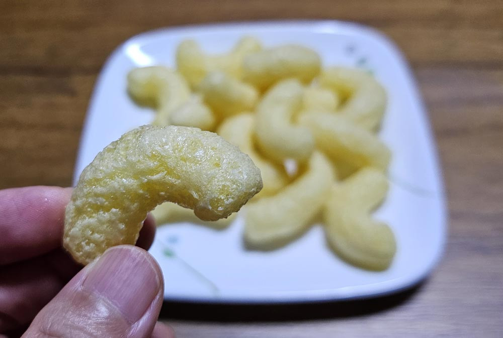 Close-up of a curved Nongshim Banana Kick corn puff held in front of a plate