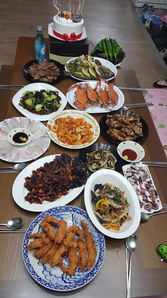 A special Korean birthday table at home with grilled meat, seafood, japchae, fried food, and a birthday cake.
